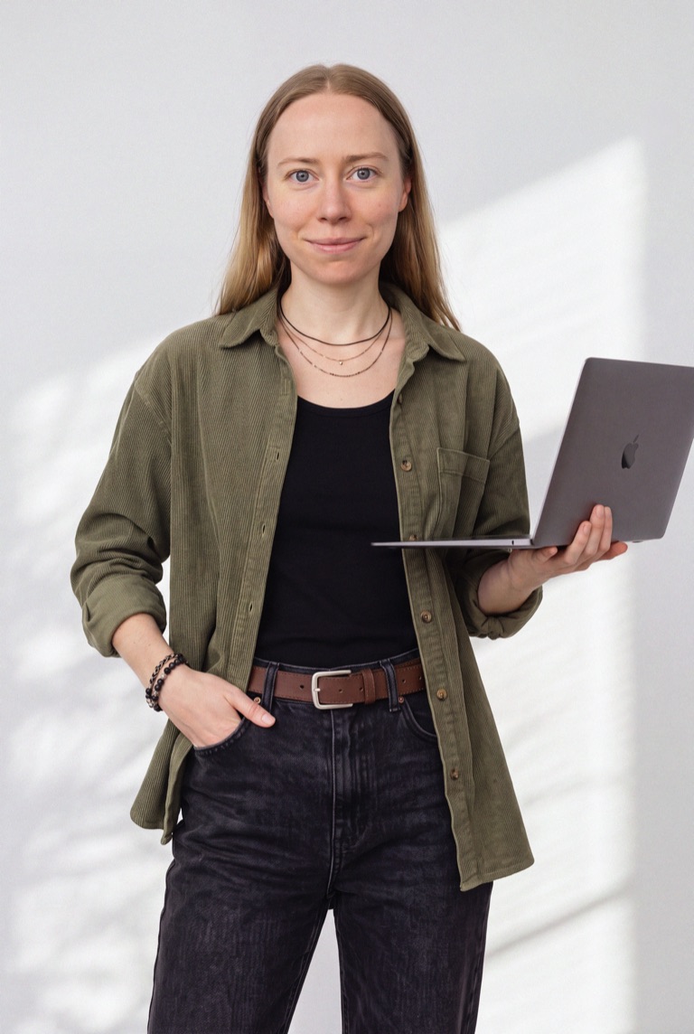 Eva Mryl, founder of Runina Creative, holding a laptop against a sunlit wall