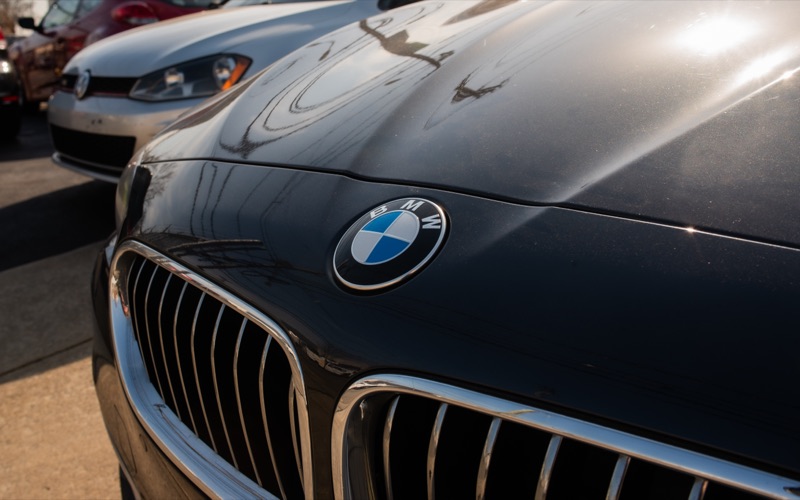 Close-up of a BMW badge and chrome grille on a dark gray hood at a dealership lot