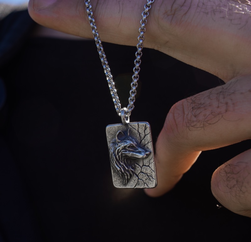 Silver wolf pendant on a chain, held in a hand against dark fabric